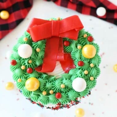 Wreath Carvel Ice Cream Cake on a white table with candies spilled around. There is a buffalo plaid napkin on the table near the cake.
