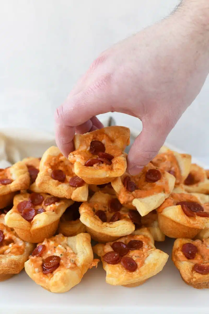 Pepperoni Pizza dough bites stacked on a white, rectangle tray with a male hand grabbing one.