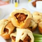 Buffalo Chicken Crescent Dough Bites on a white plate with cut celery stalks on the plate. There are black and white referee drink holders in the background.