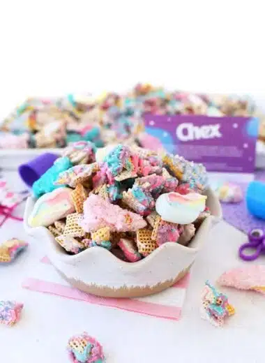 Colorful Unicorn Chex Snack Mix in a Bowl with small pieces of the mix on a white table.