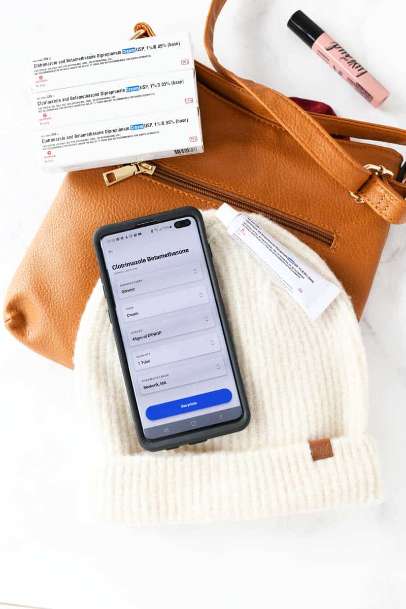 Optum Perks Savings on a black android phone. The phone is near a prescription cream, hat, and tan purse. A lipgloss is in the right of the image.