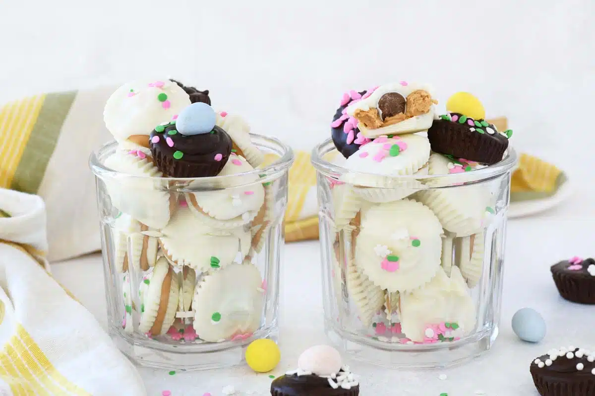 White Chocolate Peanut Butter Cups in two clear glasses. There are white and dark chocolate cups and mini eggs inside. 