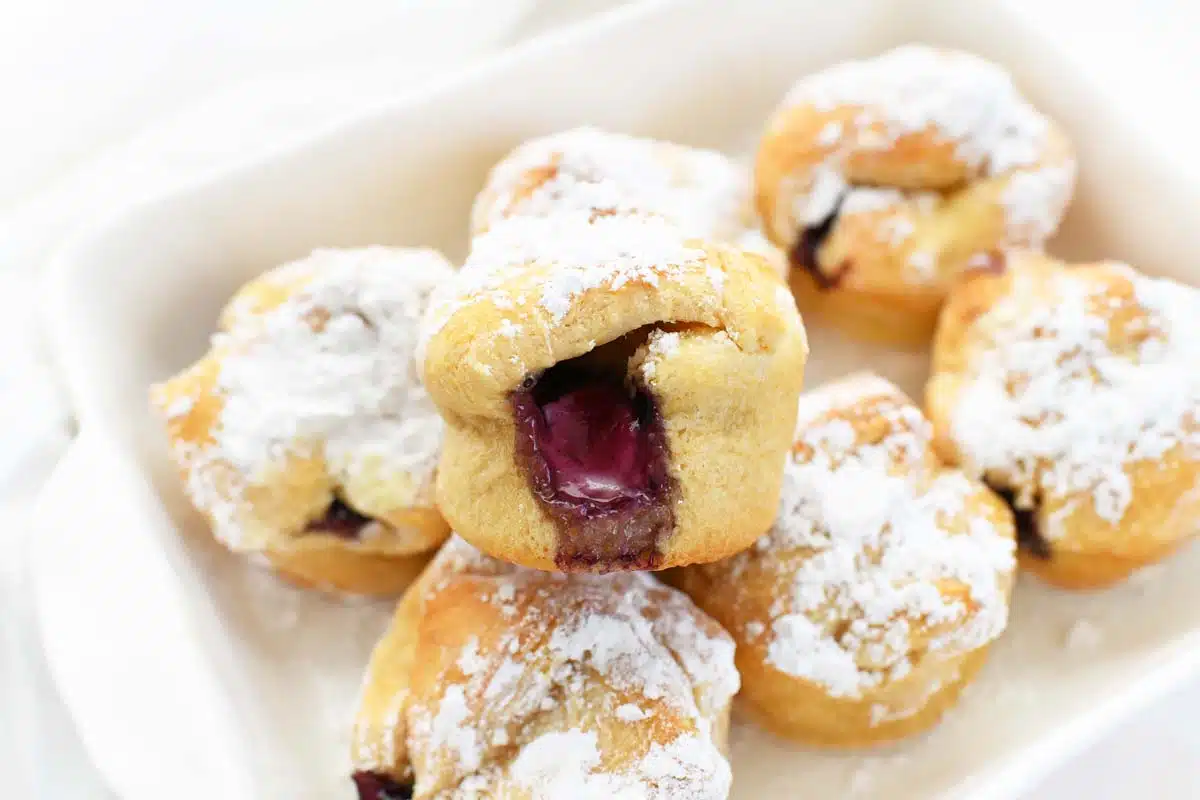 Blueberry Crescent Bites stacked in a ceramic plate with powdered sugar on top.