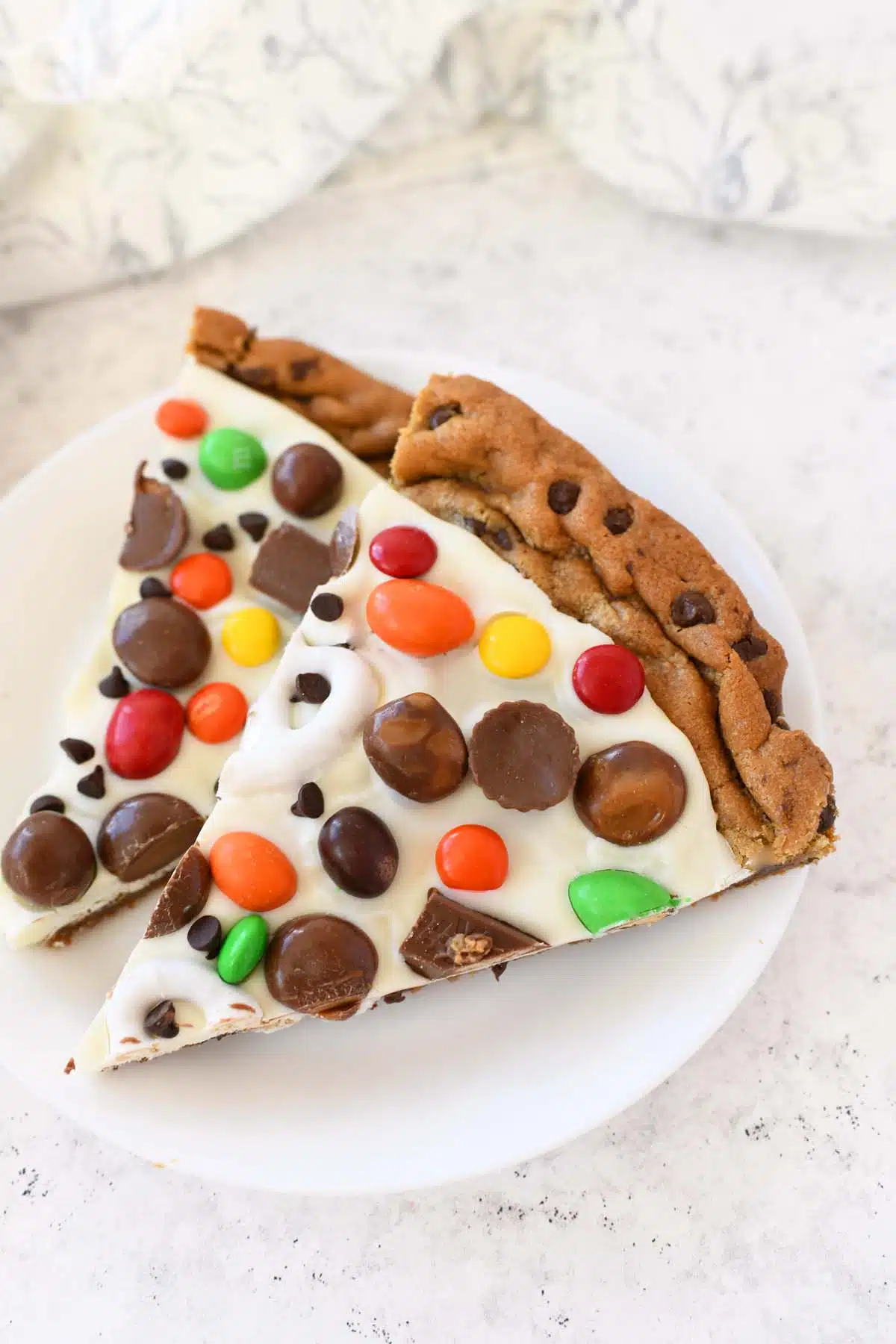 2 colorful slices of chocolate chip cookie pizza on a white plate.
