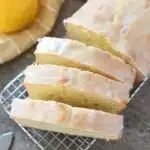 Iced Lemon Pound Cake Recipe. Sliced lemon pound cake is on a cooling rack with lemon and a yellow striped napkin nearby.