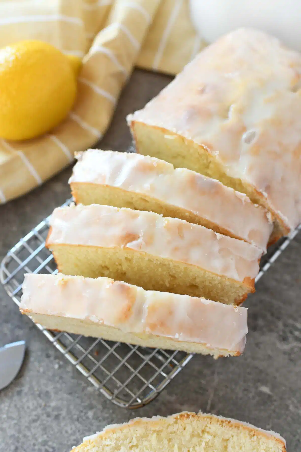 Iced Lemon Pound Cake Recipe. Sliced lemon pound cake is on a cooling rack with lemon and a yellow striped napkin nearby. 