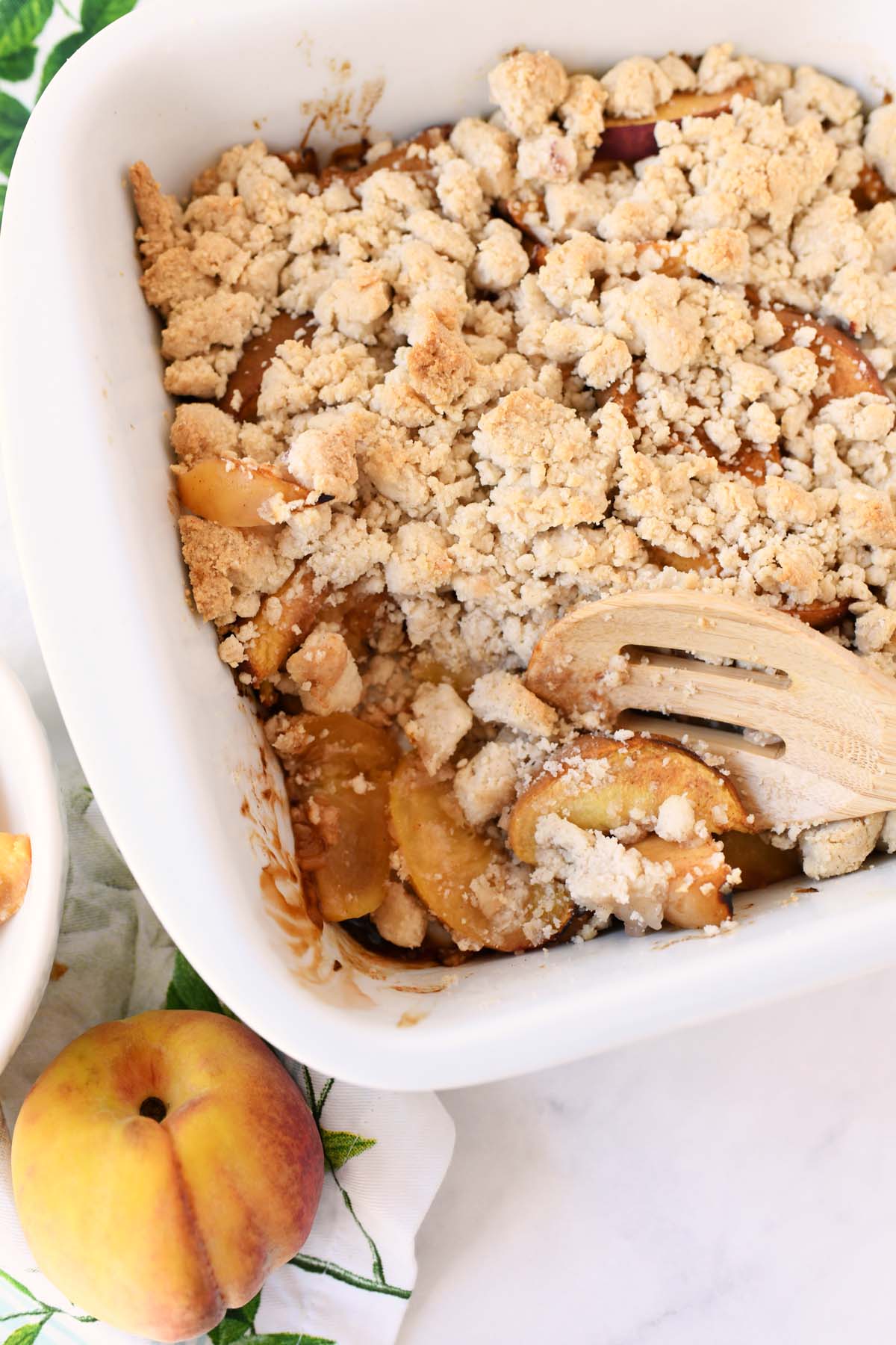 Fresh peach crumble, baked with a wooden spoon taking out some crumble from the pan.