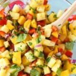 Pineapple Mango Salsa in a glass bowl with a wooden spoon.