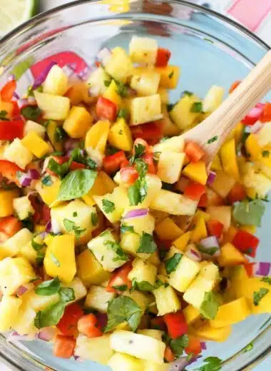 Pineapple Mango Salsa in a glass bowl with a wooden spoon.