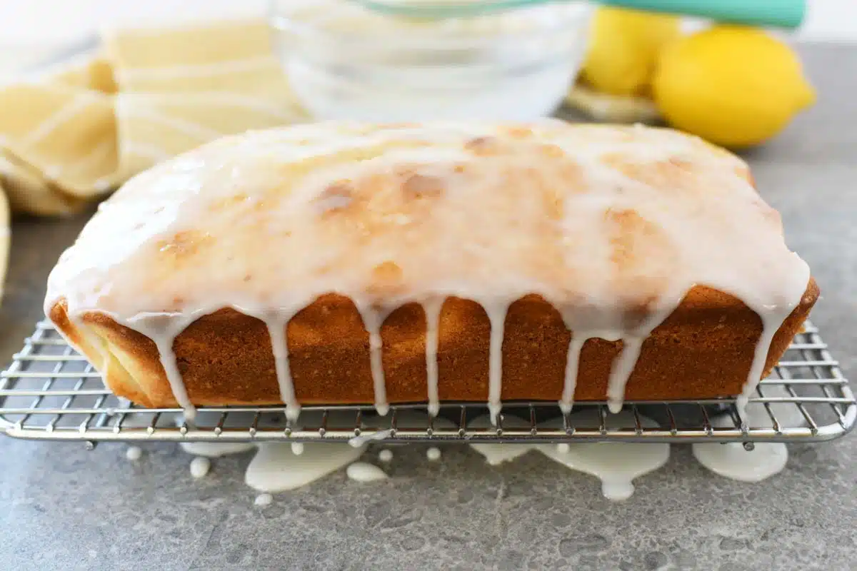 iced lemon loaf cake on a cooling rack with icing drizzling down the sides.
