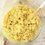 Amish Macaroni Salad in a clear, glass bowl with a wooden spoon.