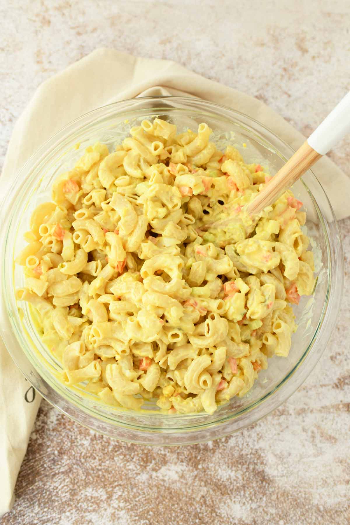 Amish Macaroni Salad in a clear, glass bowl with a wooden spoon.