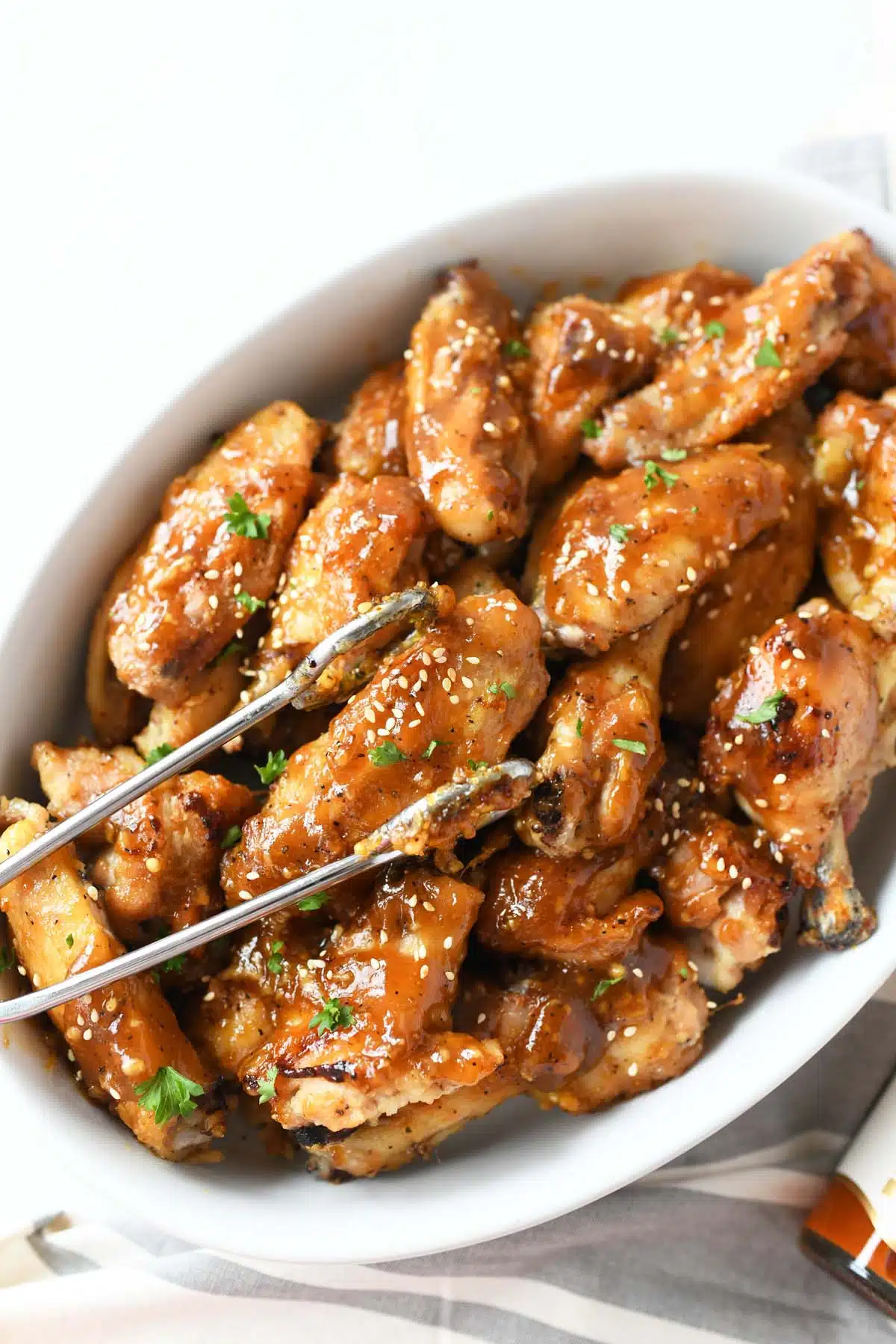 Honey Garlic Chicken Wings in a white dish with a metal tong.