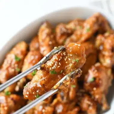 Honey Garlic Wing with sesame seeds on a metal tong.