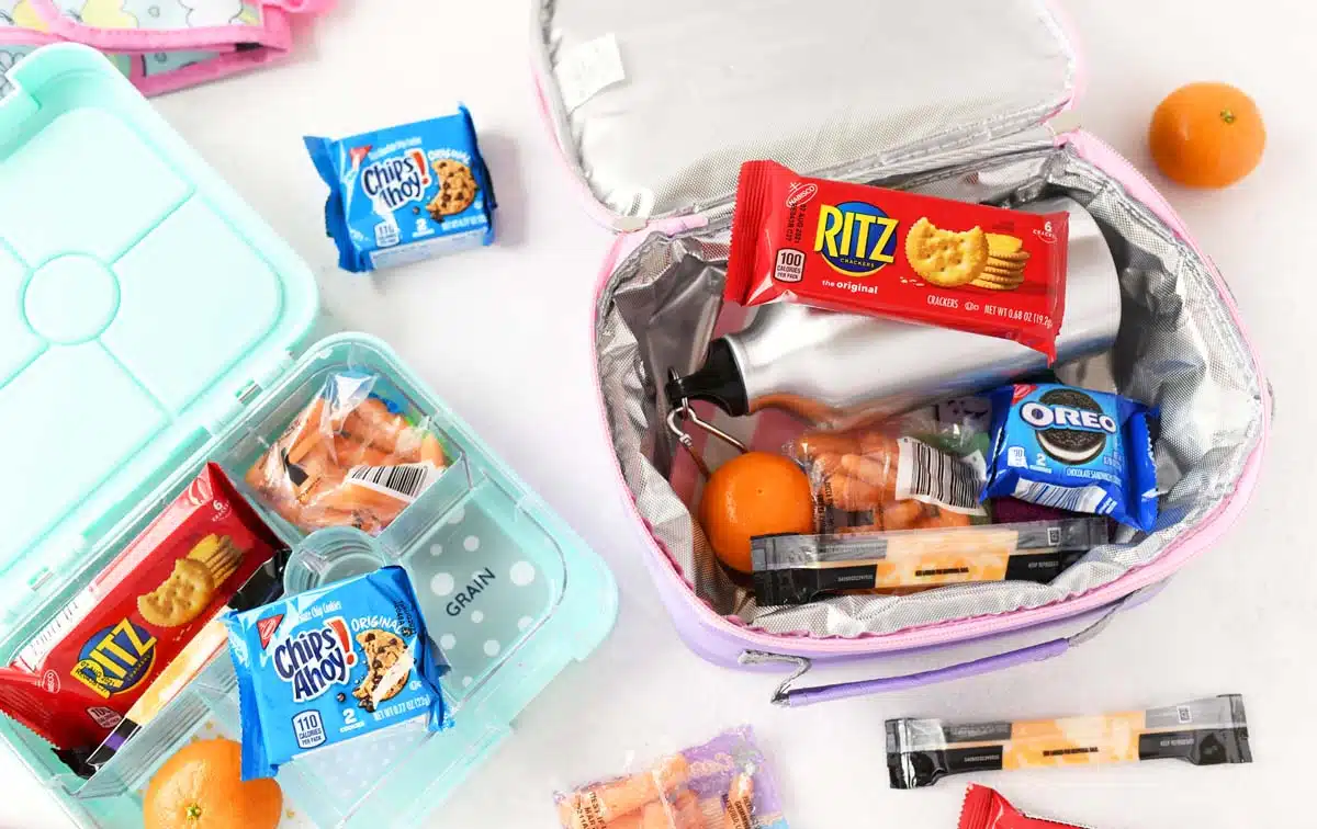 Kids lunchboxes filled with snacks like RITZ, Chips Ahoy! and mini oranges.