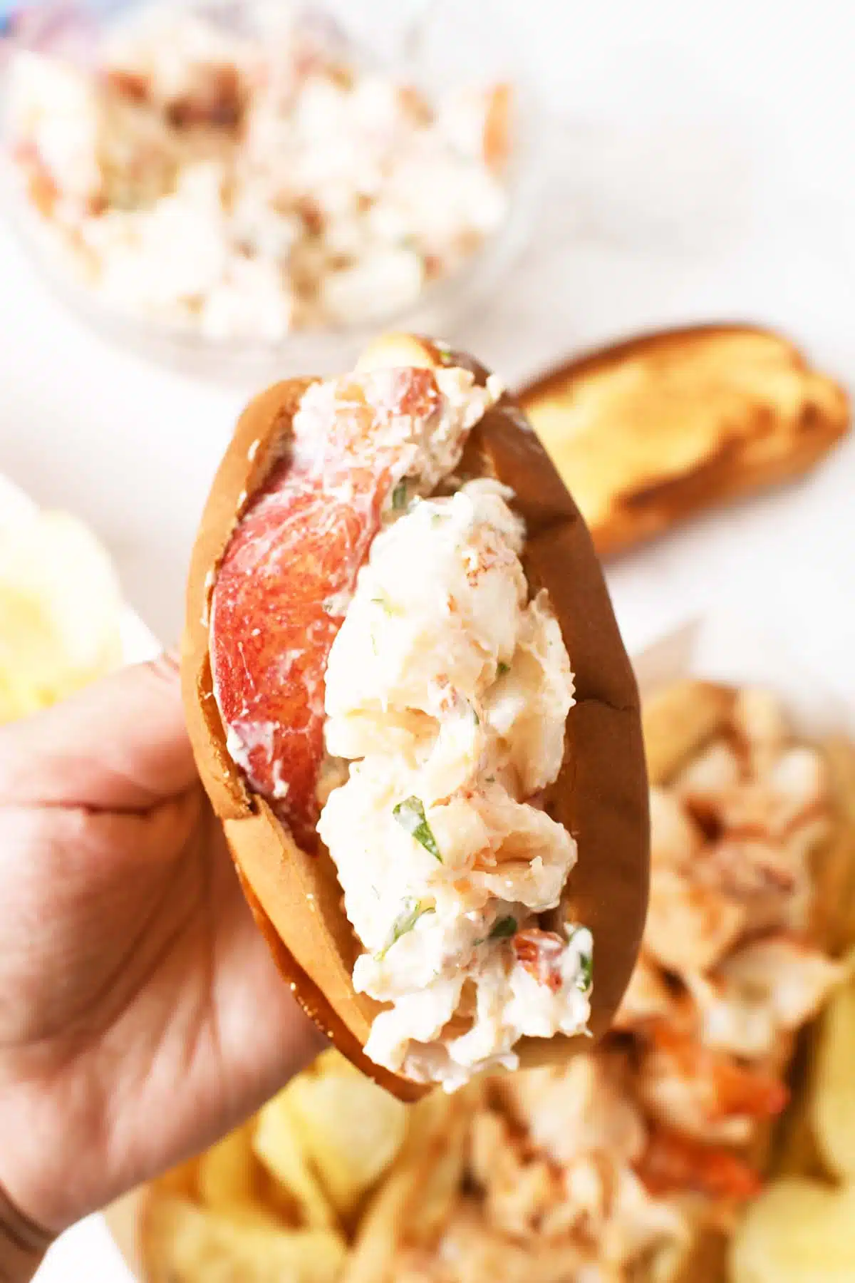 Lobster salad stuffed in a toasted min hot dog bun in a hand.