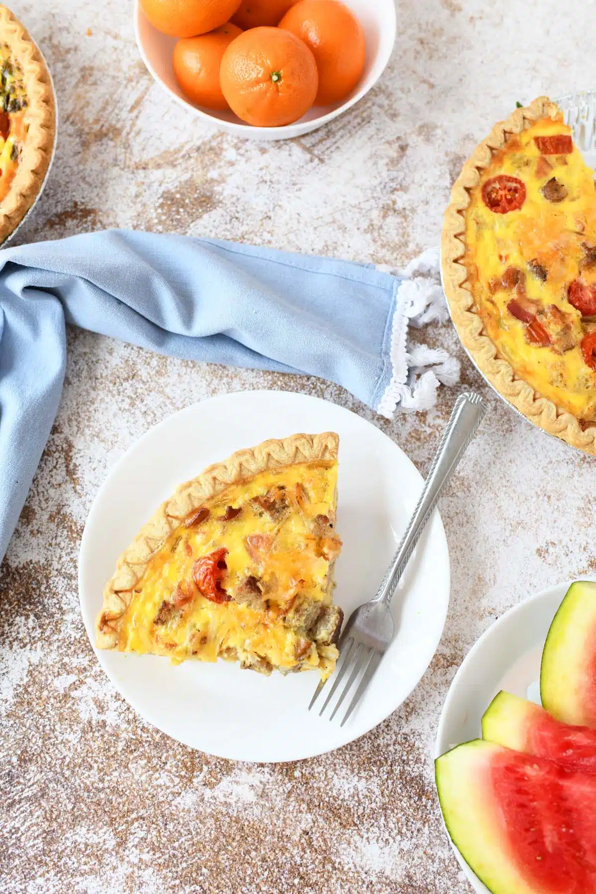 Slice of breakfast quiche on a white plate with fresh fruit around. 