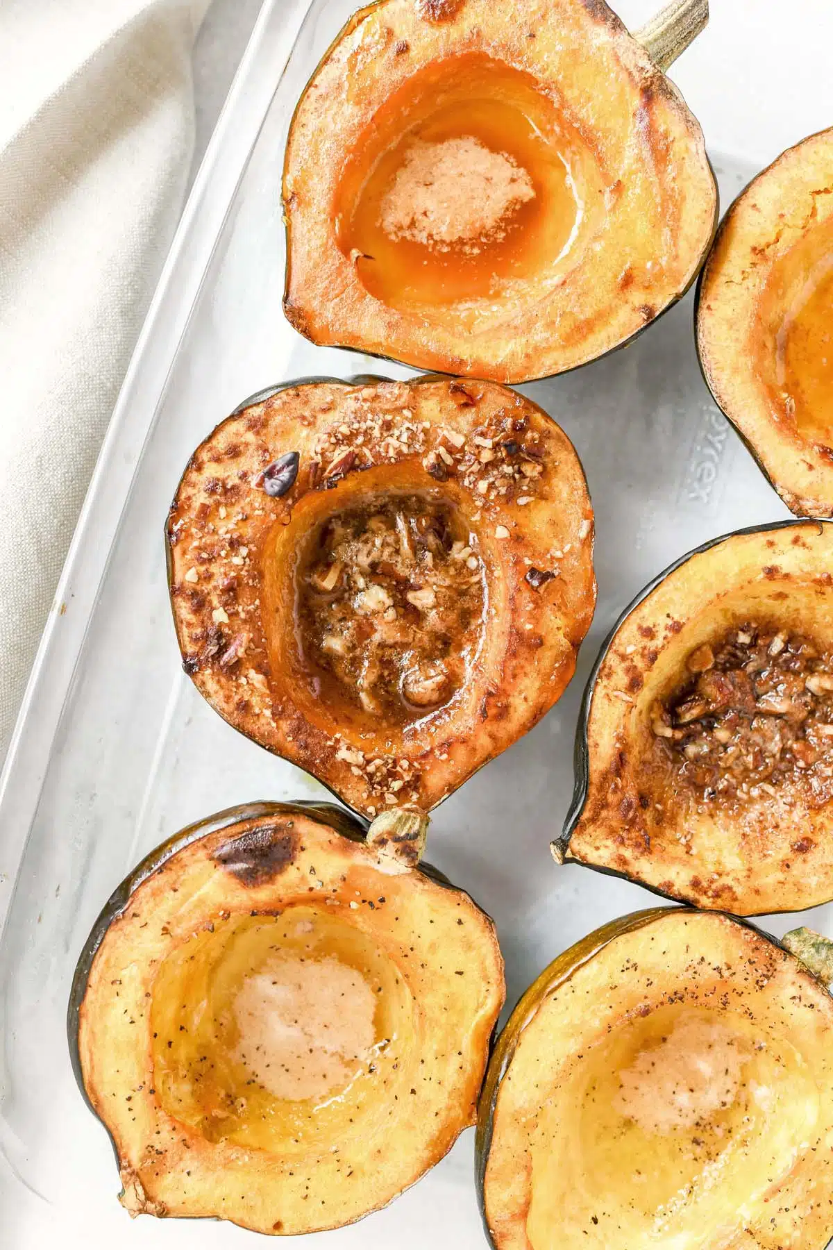 Acorn Squash roasted with butter and nuts in a clear, glass dish.