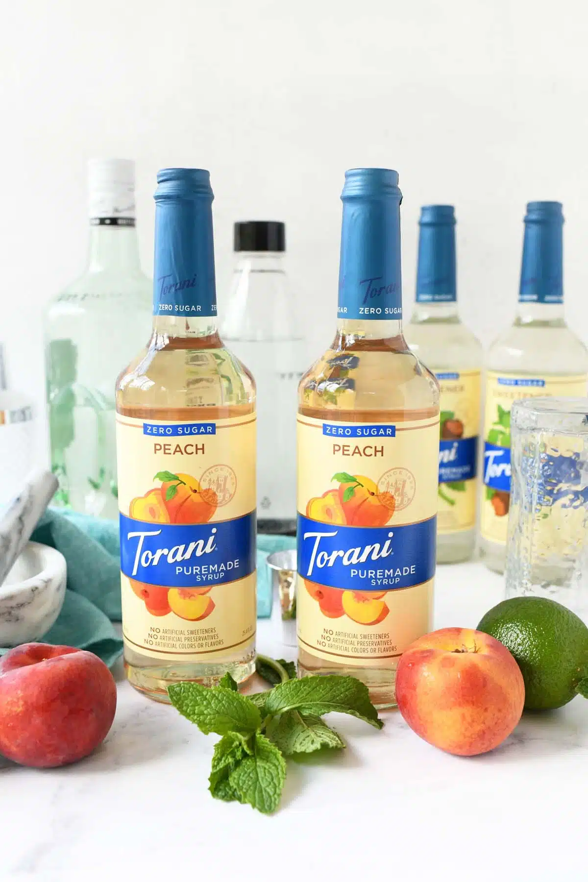 Two bottles of Torani Puremade near fresh peaches and lime.