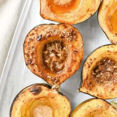 Acorn Squash roasted with butter and nuts in a clear, glass dish.