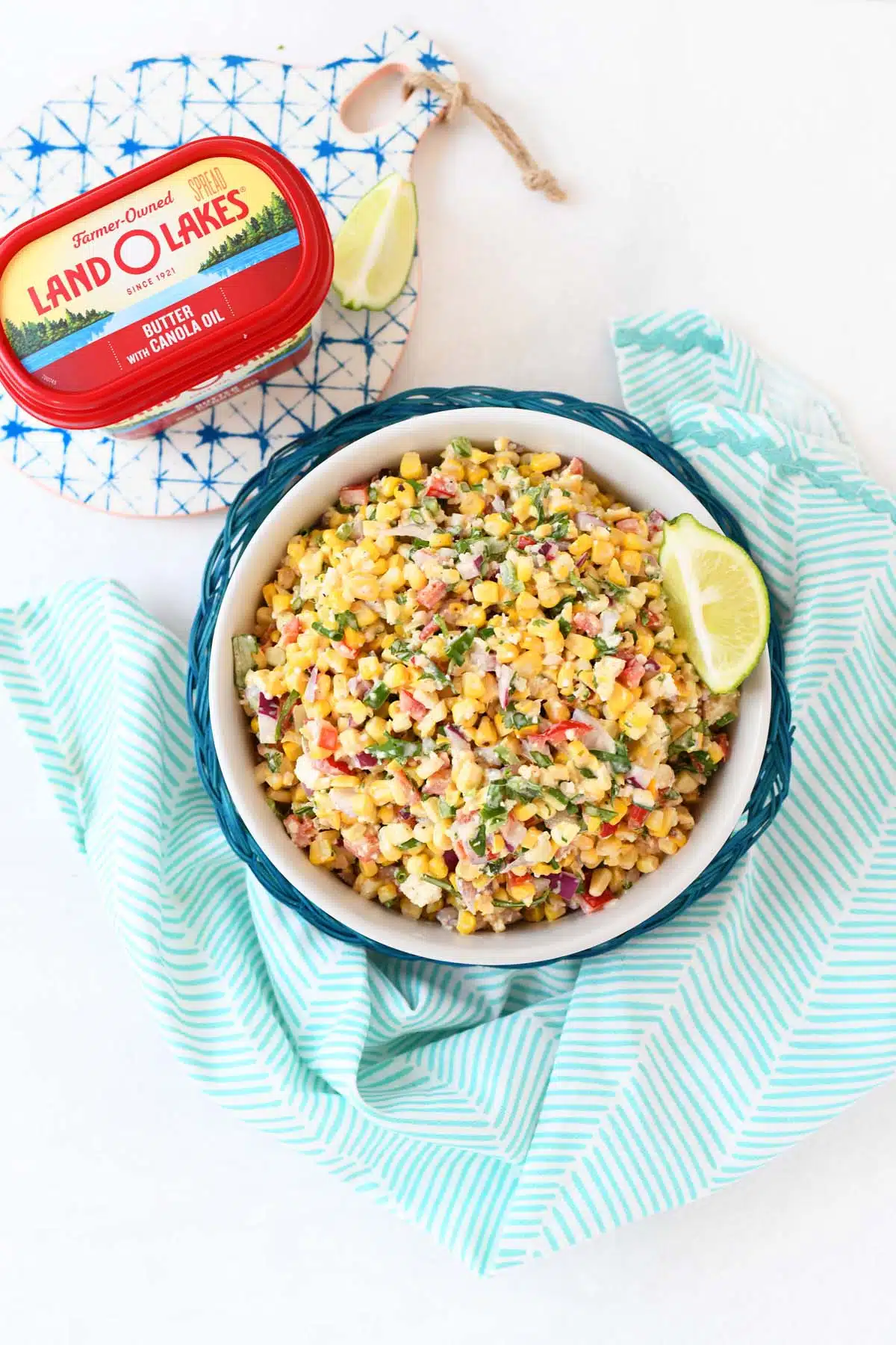 Mexican Street Corn salad in a glass bowl near a blue napkin and butter tub.