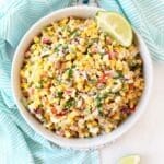 Mexican street Corn Salad with lime wedges in a white bowl.