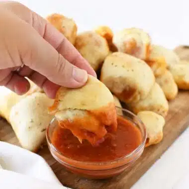A hand dipping a pizza roll into marinara sauce.
