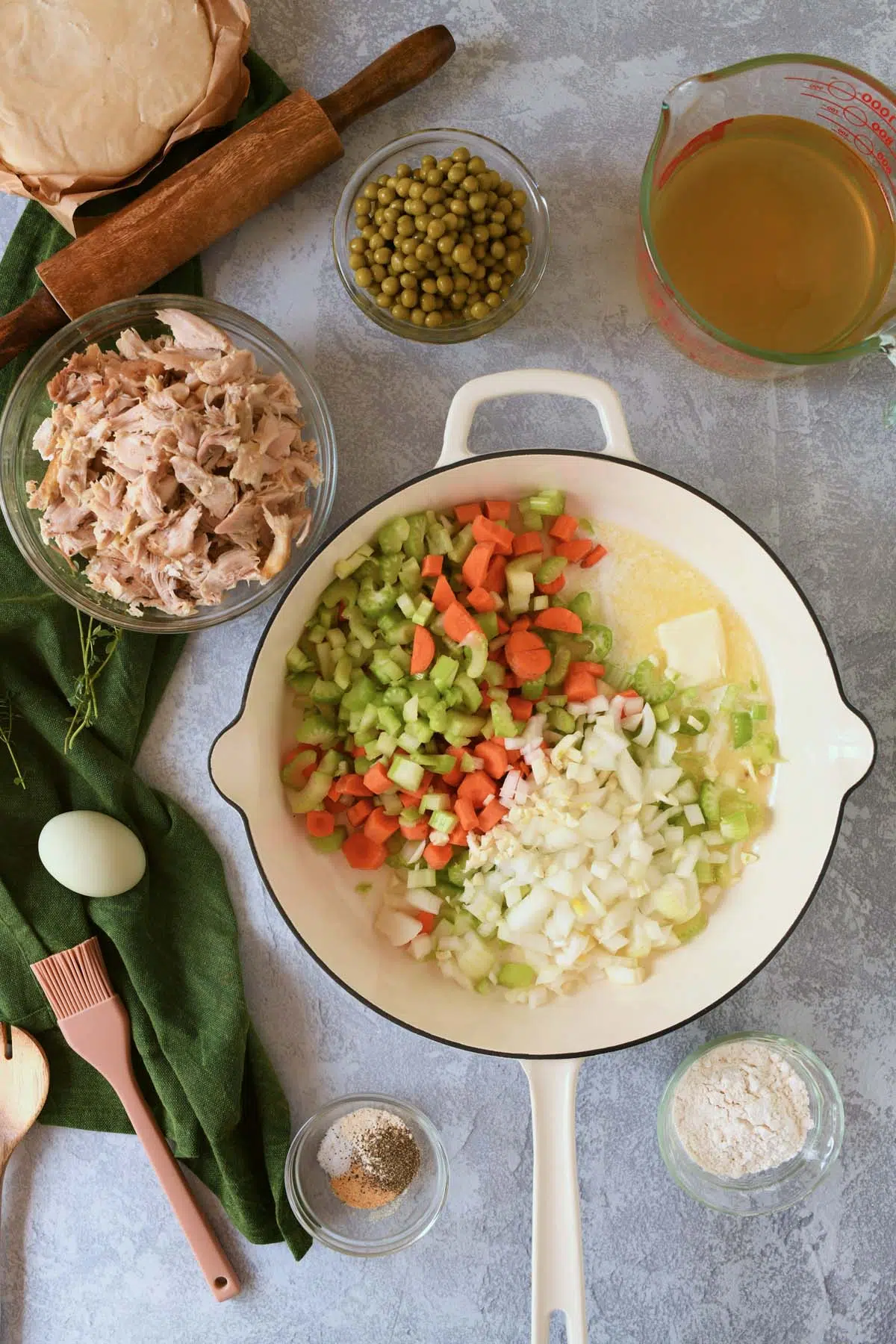 Chopped veggies in a white frying pan near other chicken pot pie ingredients.