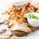 Crispy Buffalo chicken wontons on a wooden tray with dressing.