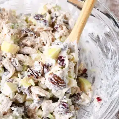 Fall Apple Pecan Chicken Salad in a glass bowl with a wooden spoon.