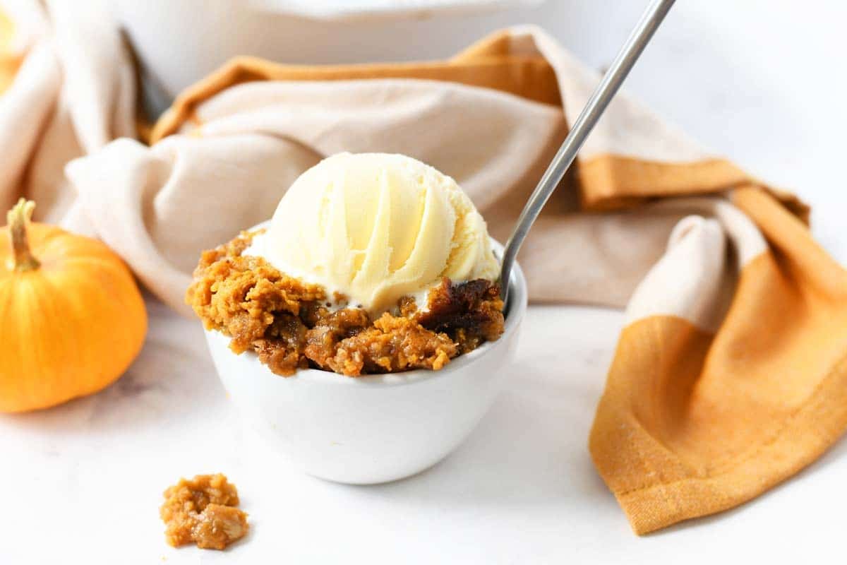 Pumpkin Crisp in a white bowl with ice cream and a silver spoon.