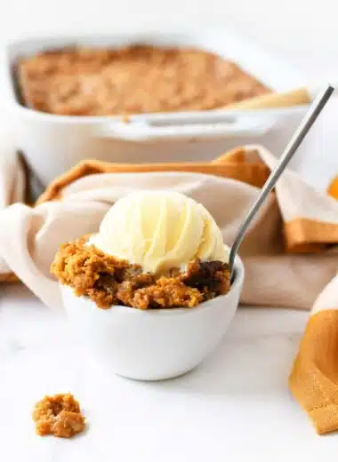 A bowl of warm pumpkin crisp with vanilla ice cream.