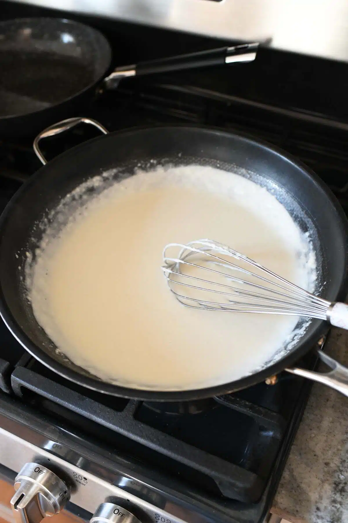 Béchamel Sauce with a wire whisk in a black skillet.