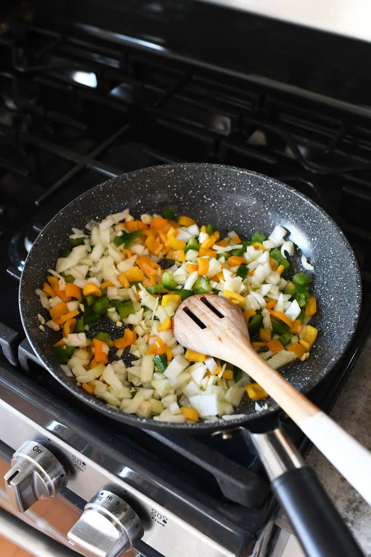 Chopped veggies in a black skillet with a wooden spoon.