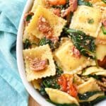 Bacon spinach ravioli in a white dish with a blue napkin.
