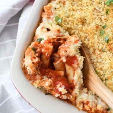 A wooden spoon is a red, saucy pan of chicken parmesan casserole.
