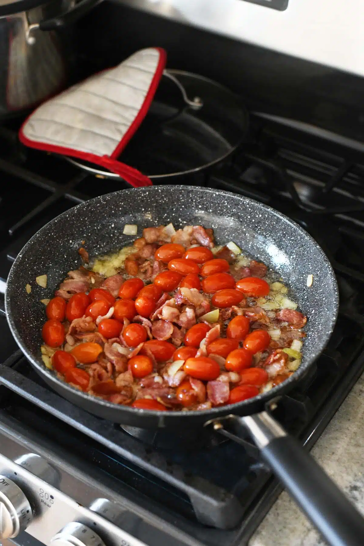 tomatoes and onion in a grey skillet.