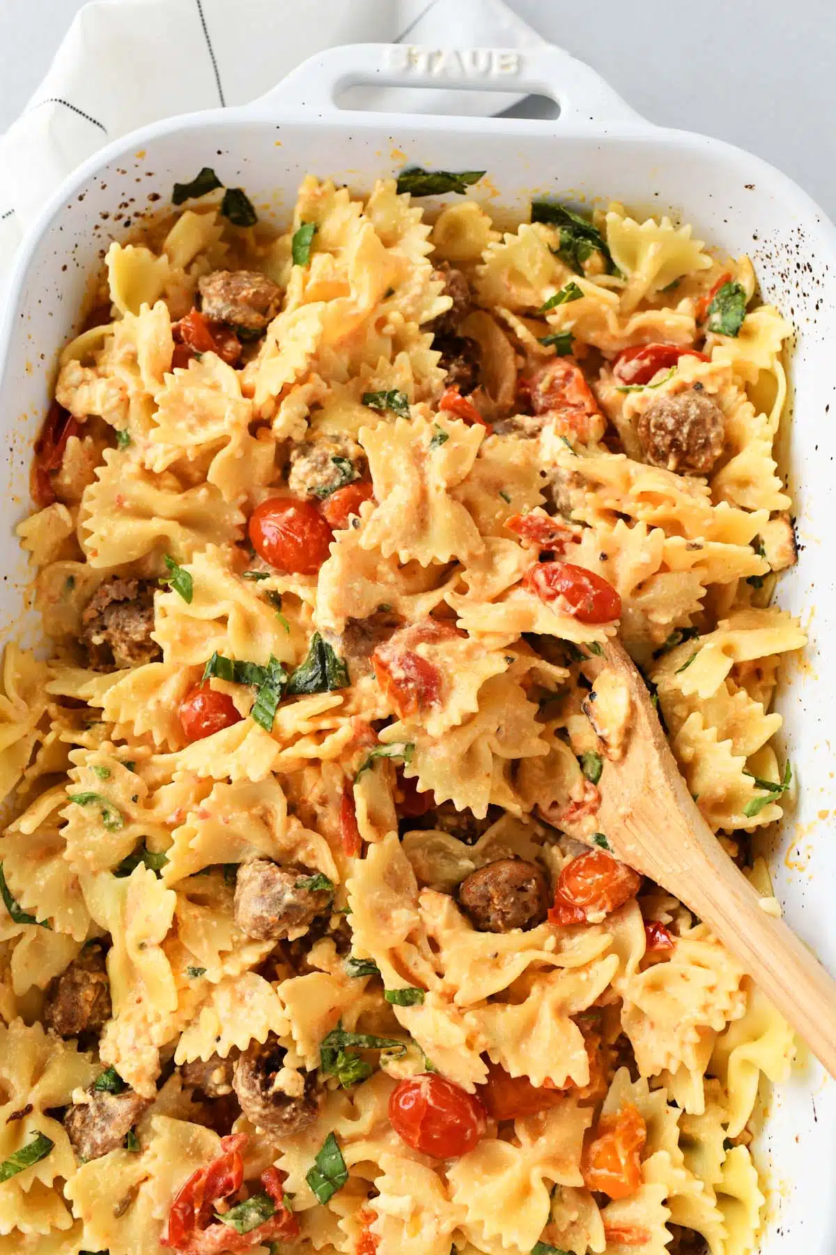 A wooden spoon inside sausage and feta pasta.