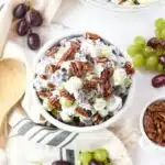 Grape salad with pecans in a small white bowl with small piles of grapes nearby.
