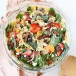 A colorful bowl of beautiful strawberry salad with a pink napkin and wooden spoon.