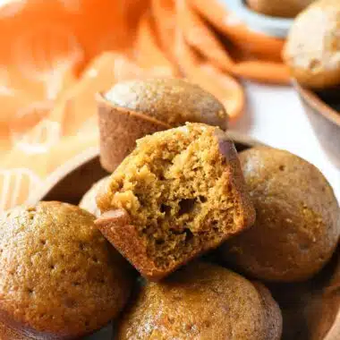 A fluffy, bitten pumpkin spice muffin in a wooden bowl.
