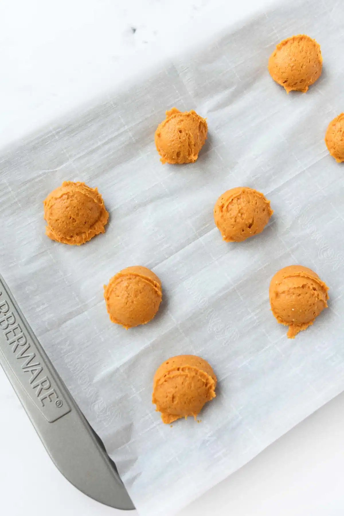Mounds of pumpkin cookie dough on a cookie sheet.