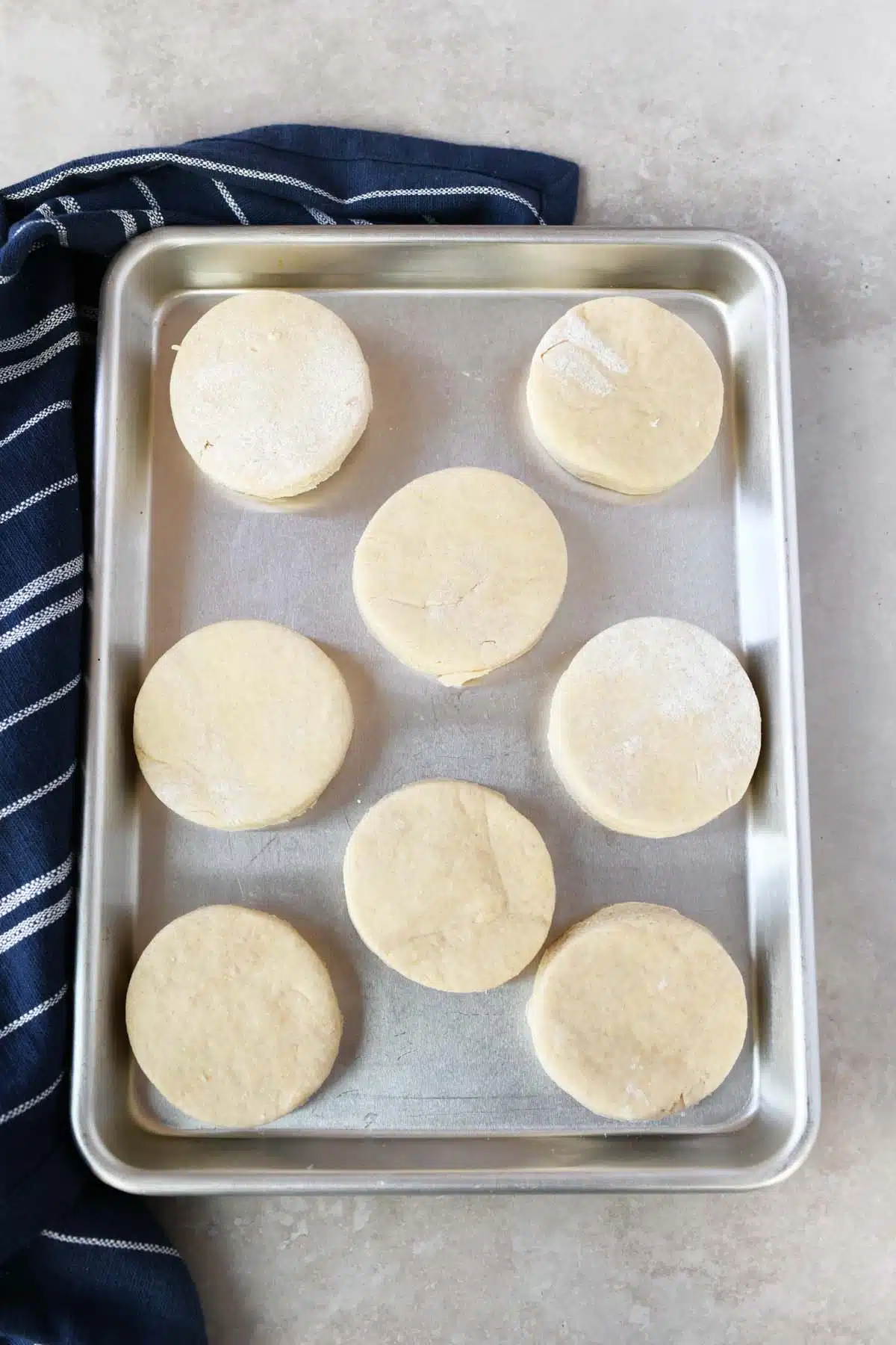 Biscuit dough circles on a stainless steel baking tray.