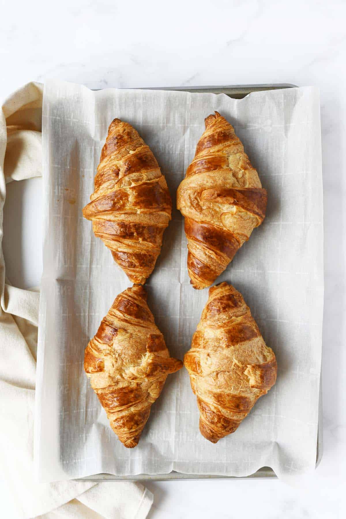 Four baked croissants on a parchment-lined baking sheet.