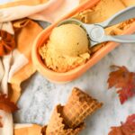 Pumpkin ice cream near cones and fall leaves.