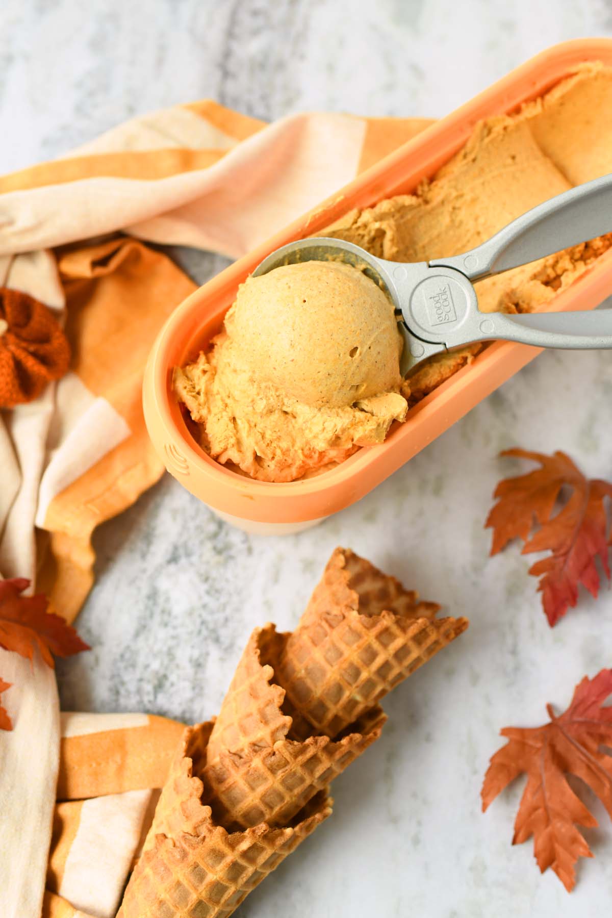 Pumpkin ice cream near cones and fall leaves.
