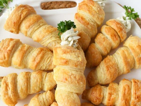Puff pastry carrot appetizers on a white tray.
