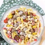 A glass bowl of Italian pasta salad with a green, floral, napkin.