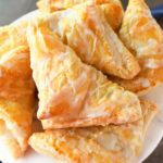 A white plate of golden-brown iced lemon turnovers.