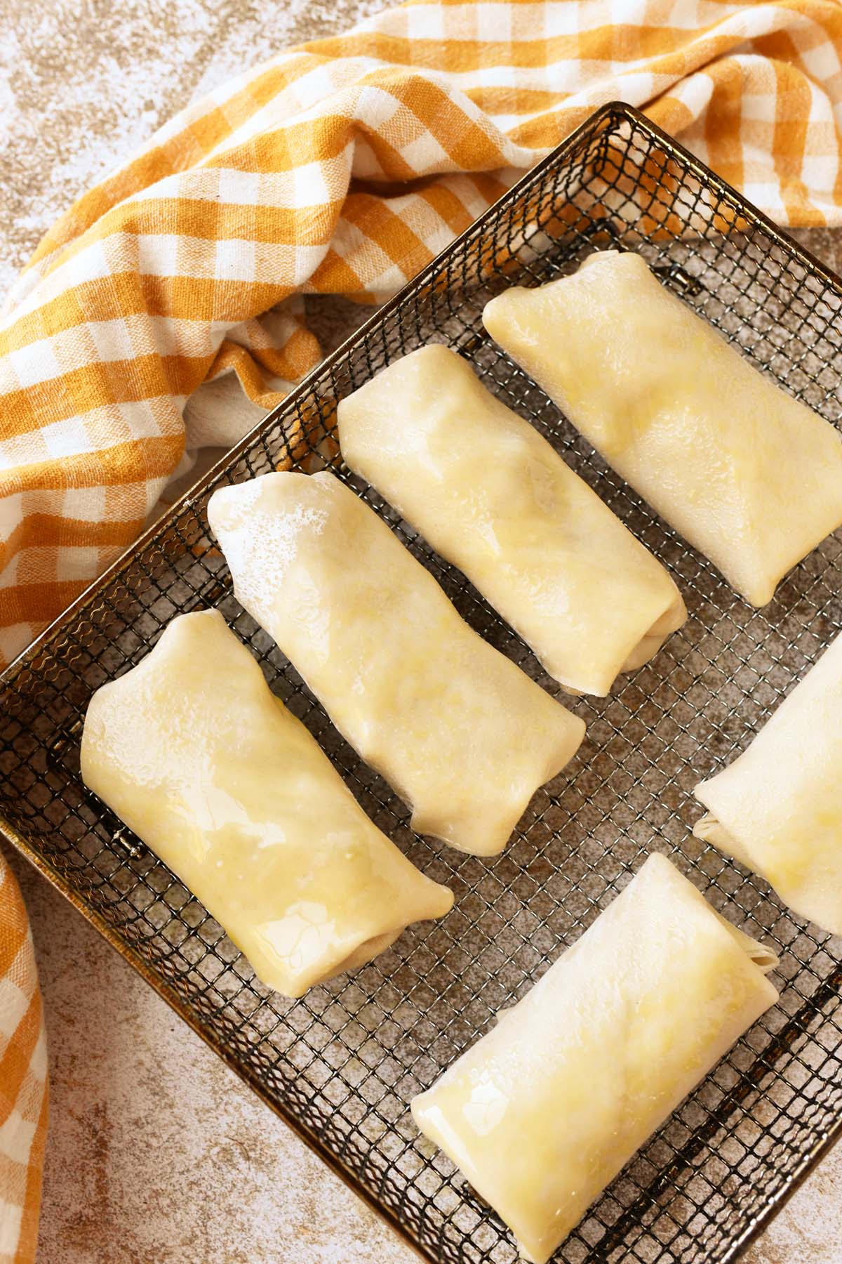 Uncooked apple pie egg rolls on a silver air frying tray.